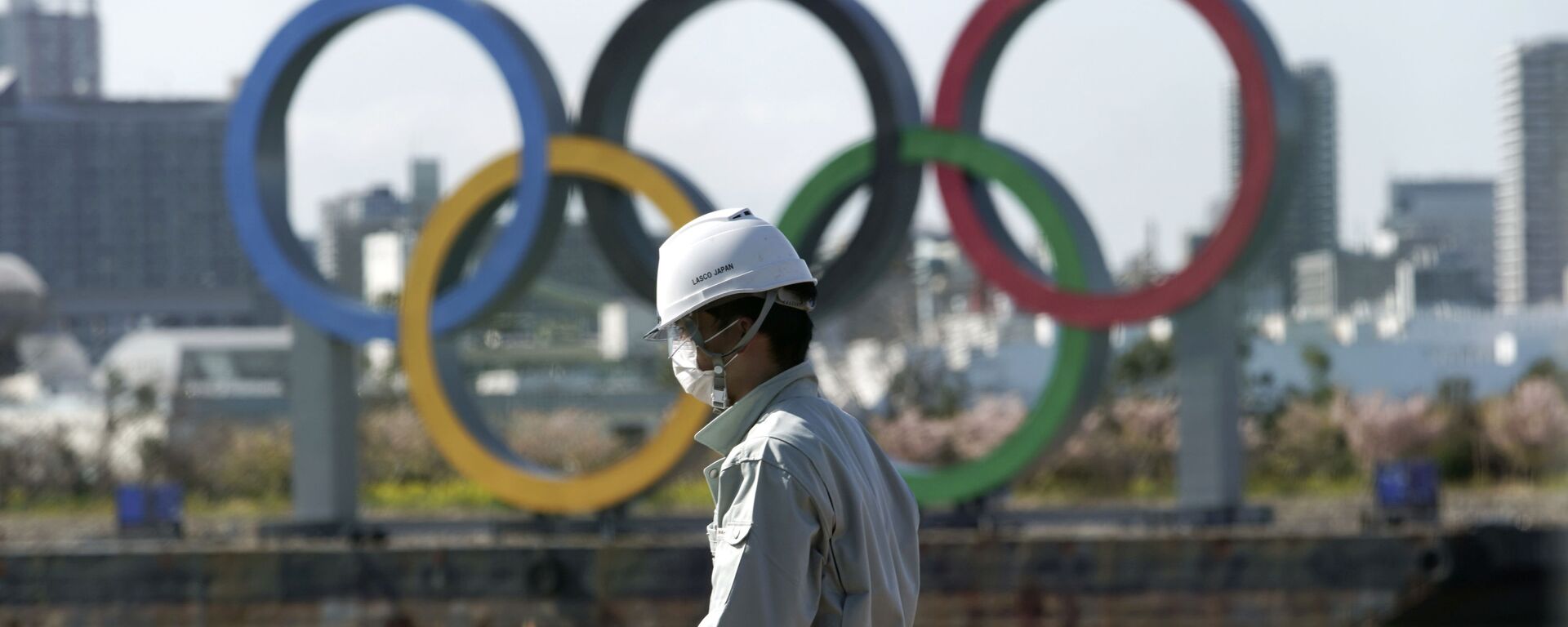 Човек с маском испред олимпијских кругова у Токију. - Sputnik Србија, 1920, 24.03.2022