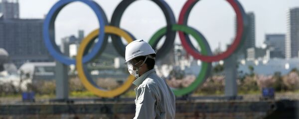 Čovek s maskom ispred olimpijskih krugova u Tokiju. - Sputnik Srbija