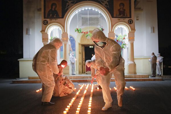 Volonteri u zaštitnim odelima za vreme uskršnje službe u Rumuniji. Sveštenici su u pratnji volontera zapalili sveće u ponoć na pravoslavni Uskrs pošto vernicima nije bilo dozvoljeno da prisustvuju liturgiji. - Sputnik Srbija
