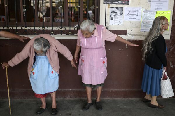 Starije žene održavaju udaljenost jedna od druge dok čekaju da se upišu u državne programe socijalne pomoći u centru Ozumba, u Meksiku, 3. aprila 2020. godine, za vreme izbijanja pandemije novog virusa korona.
 - Sputnik Srbija