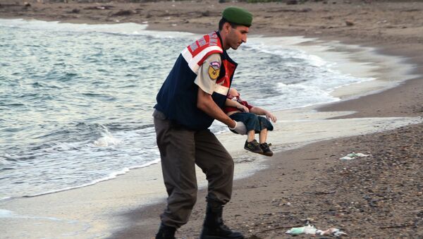 Турски полицајац носи тело трогодишњег дечака, избеглице из Сирије Ајлана Курдија - Sputnik Србија