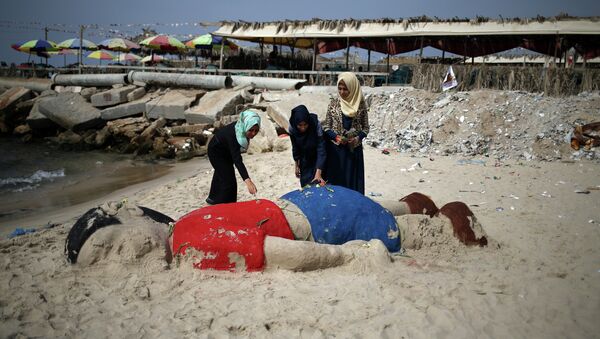 Mlade Palestinke na plaži u Gazi položile cveće na peščanu skulputuru sirijskog dečaka Ajlana Kurdija, trogodišnjeg dečaka koji se utopio u Turskoj u izbegličkom zbegu - Sputnik Srbija